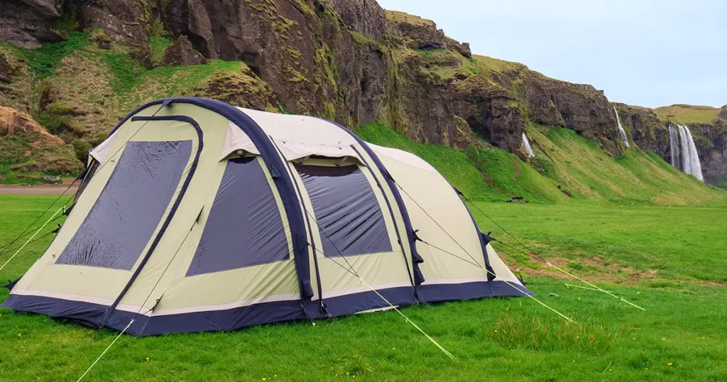 Wild camping with waterfalls in the background. Big tent near mountains, Iceland