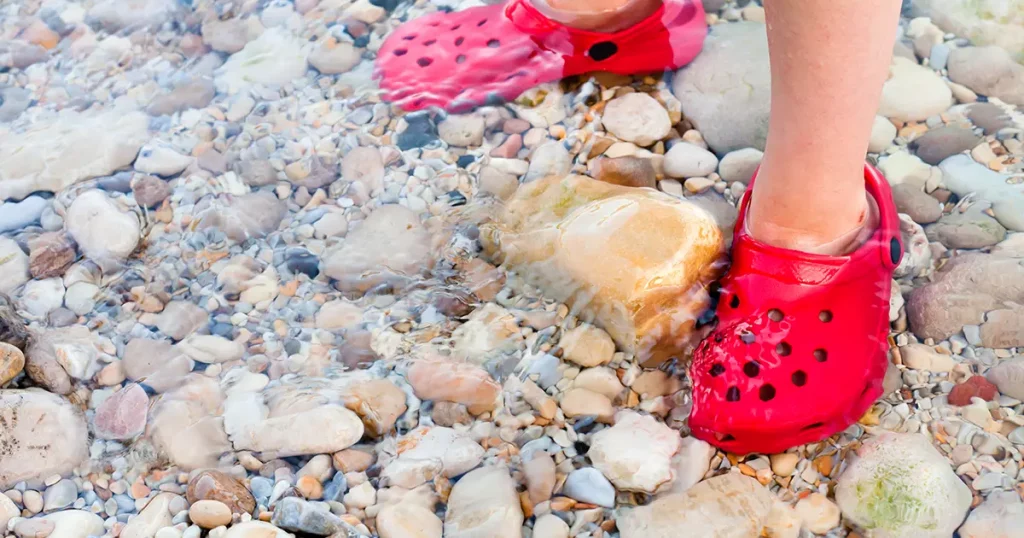 Child standing in shallow water with nice red shoes