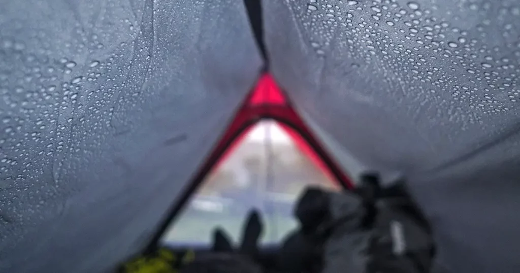 Man lying inside a tent on a rainy day with water drops on the walls