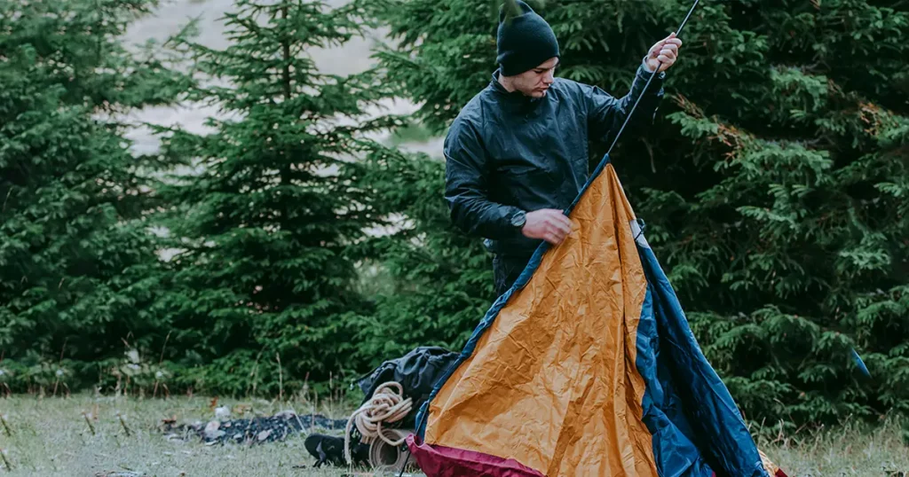 A male hiker is setting up a bright orange, blue and red tent in the forest
