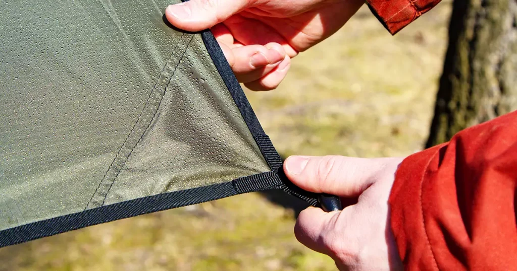 Close-up of male hands and the corner of an tarp with a grommet