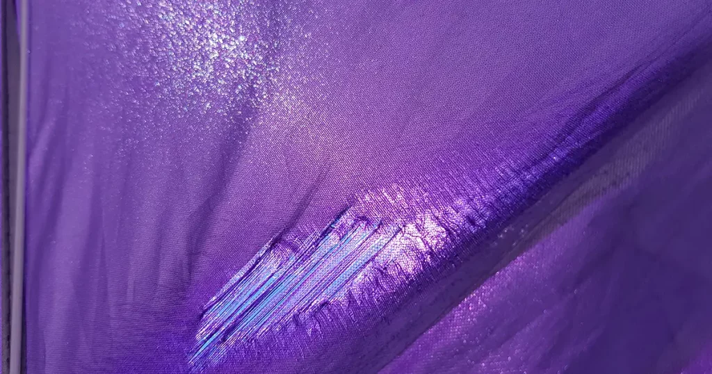 Purple lacerated fabric surface with worn textile structure closeup