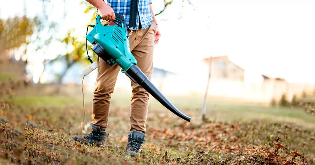 Gardener clearing up leaves using an electric leaf blower tool. Gardening details