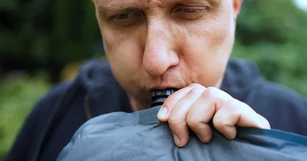 Close up of man blowing up a self inflatable sleeping pad for camping