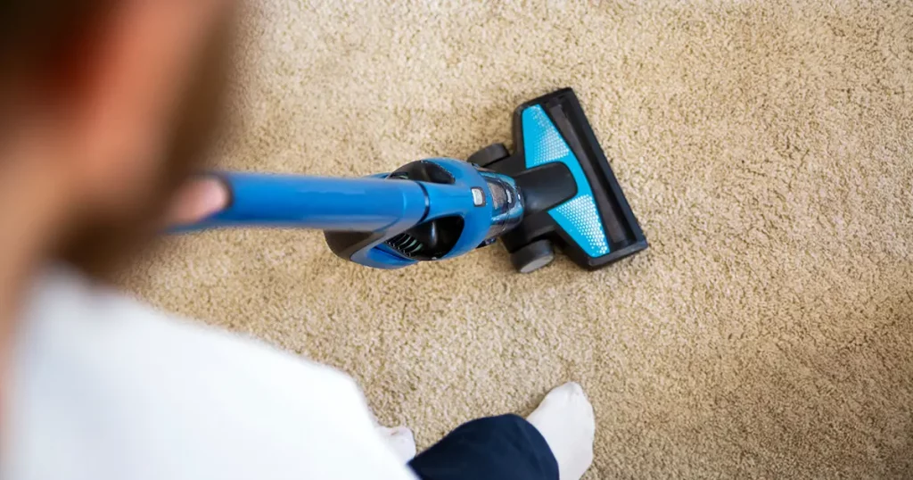 Vacuuming a carpet with a handheld vacuum cleaner, top view.