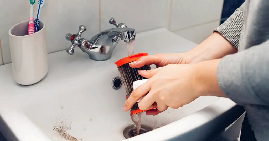 Woman washing dirty filter with water and soap in bathroom sink at home. Hosehold chores