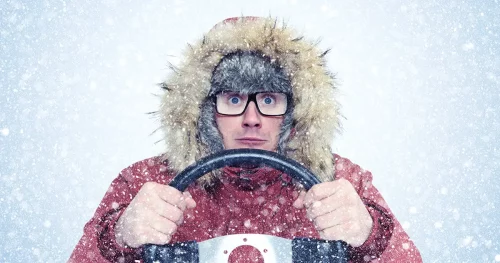 Man in winter clothes with a steering wheel, snow blizzard. Concept car driver
