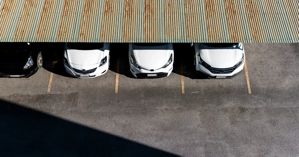 4 cars under neat a metal car shelter with the sun shining on them