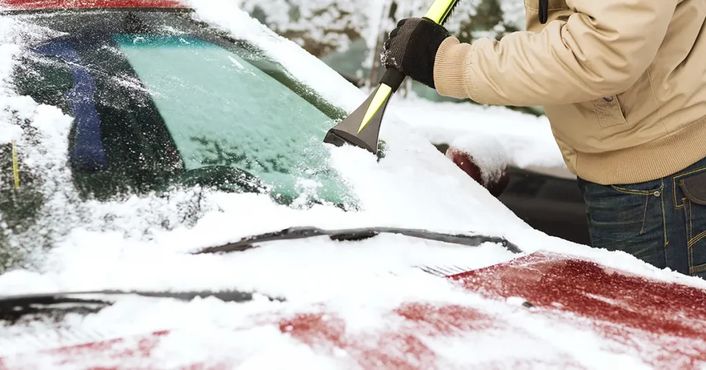 man scraping ice from car windshield with brush