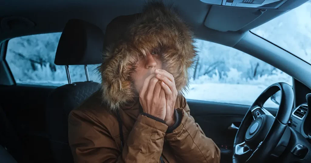 Man in down jacket tries to keep warm and not freeze in his stalled car in winter