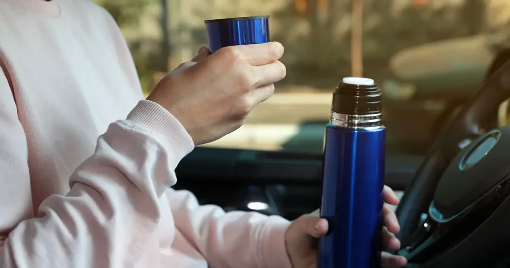 Woman with thermos on driver's seat of car, closeup