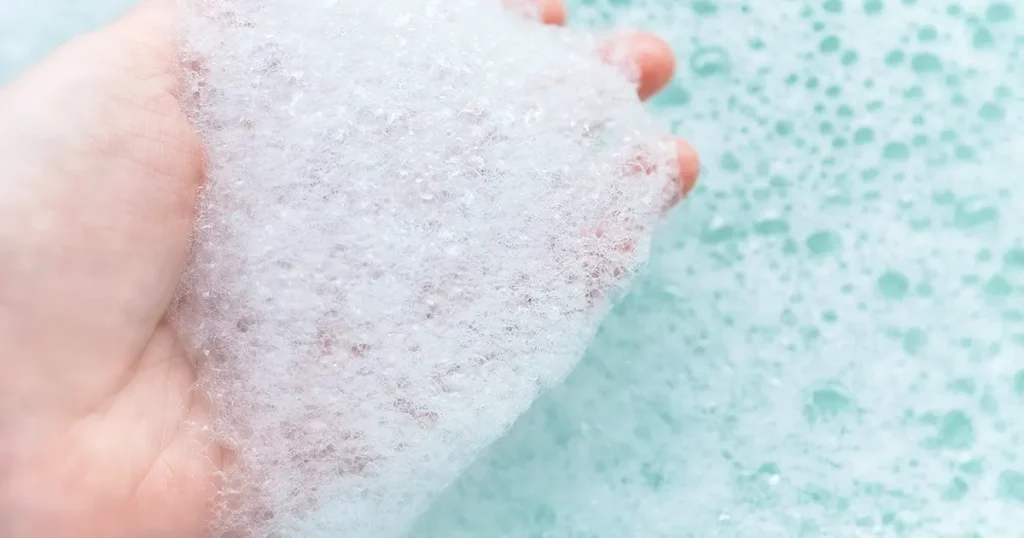 Hand with white foam soap bubbles.