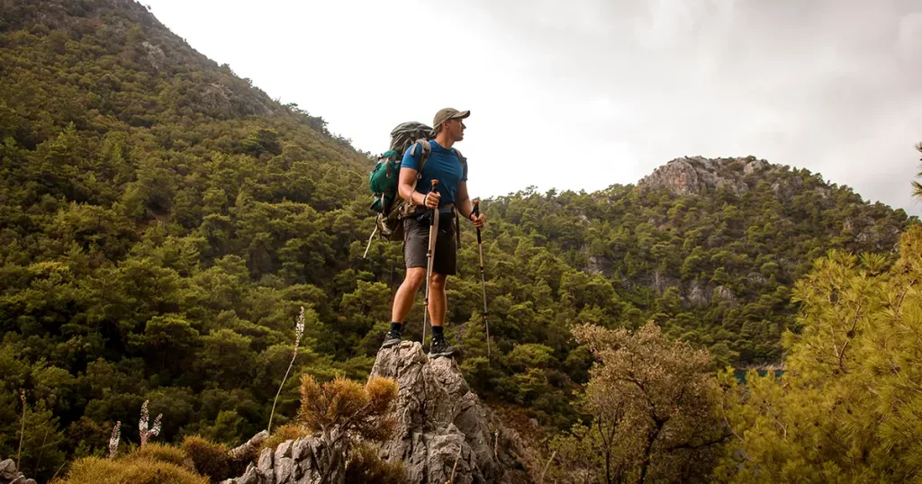 male tourist with trekking poles and backpack stands on hill