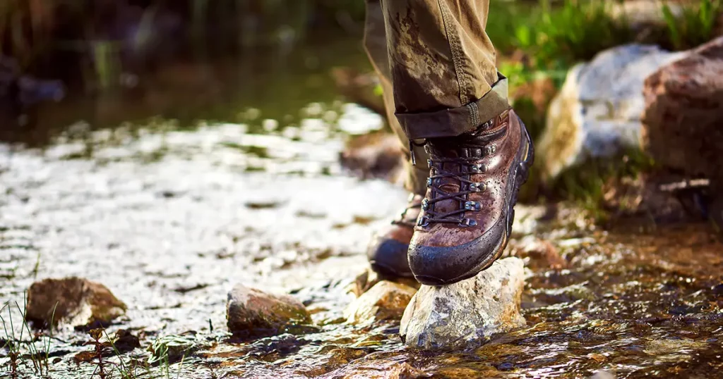 The trekker stands on the rocks in a small creek, trekking shoes