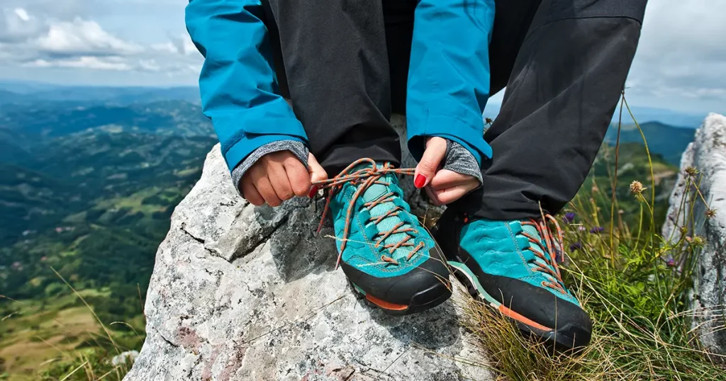 Young female tying shoelaces on a beautiful mountain top.