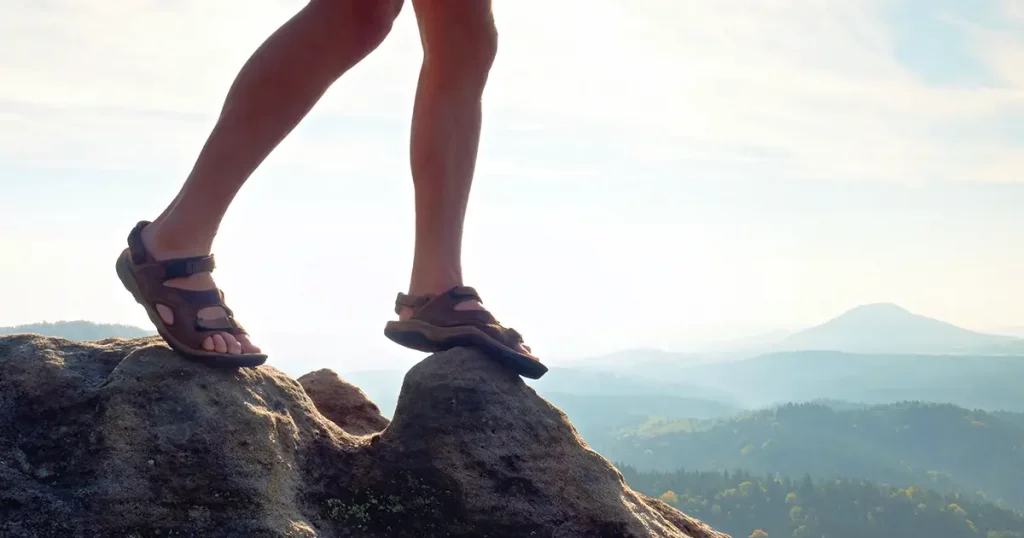 Long tired naked legs in hiking sandals on peak