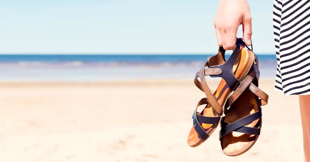 Woman on the beach holding her sandals at sunny summer day