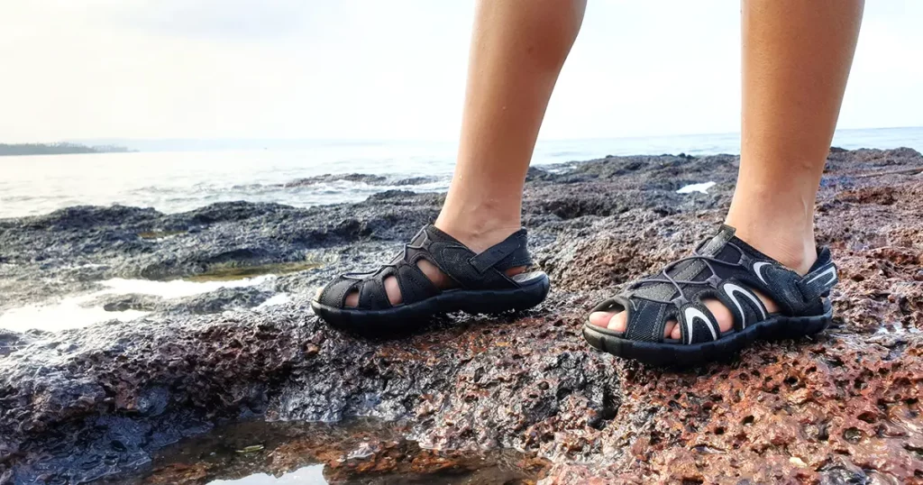 Close up of female legs wearing washable waterproof sport sandals standing on the rock near sea.