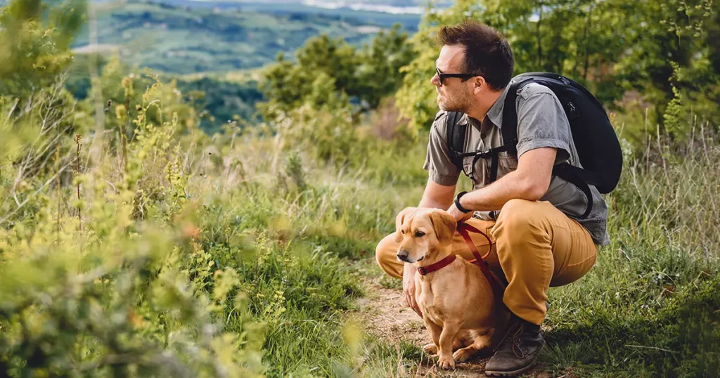 Man wearing sunglasses with a small yellow dog resting at the hiking trail