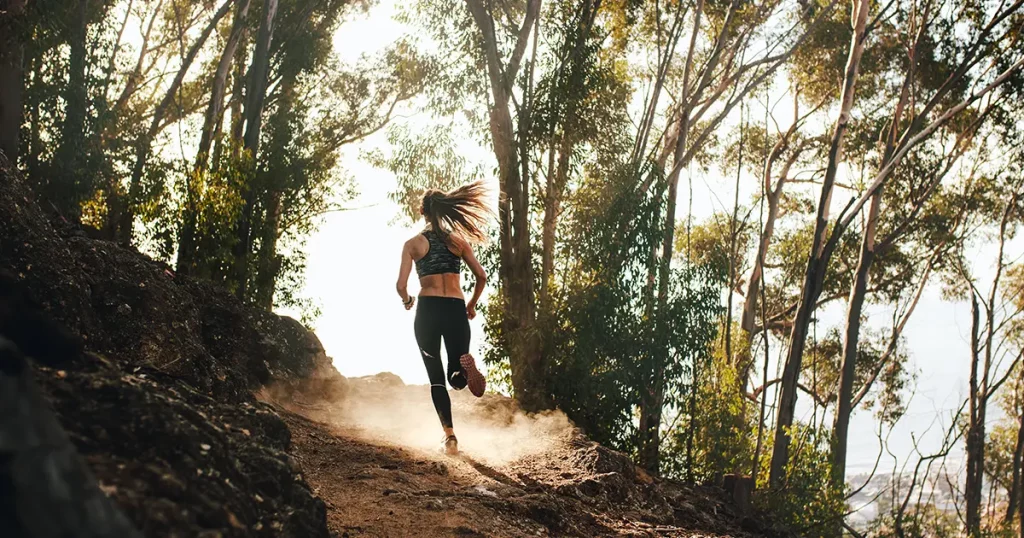 Rear view of woman trail running on a mountain path. Runner working out in beautiful nature.
