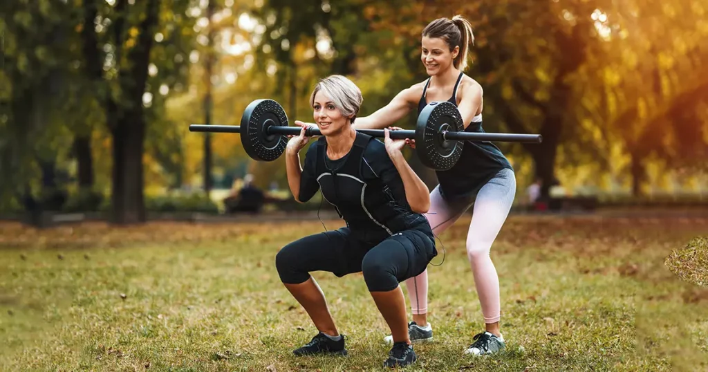 woman is doing squat exercises with personal trainer in the park