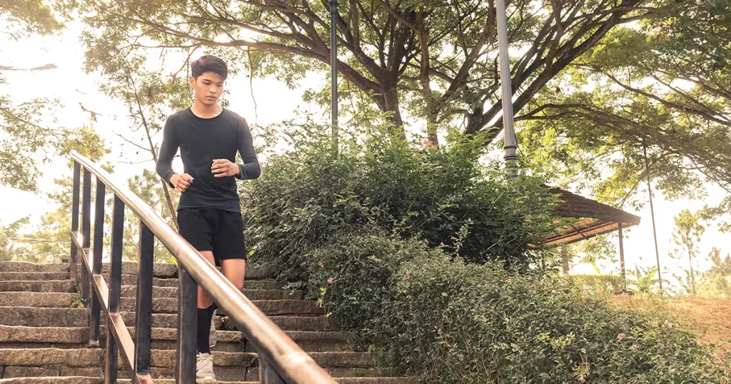 A young man runs down a flights of steps at a downhill slope. Outdoor exercise scene.