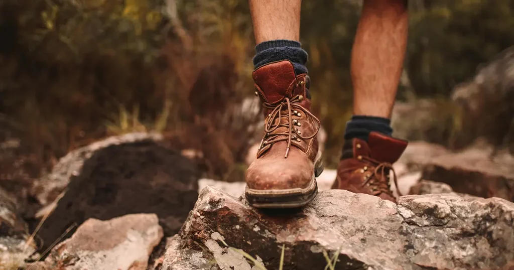 Closeup of male hikers shoes on rocky trail. Man walking through rugged path wearing trekking boots.