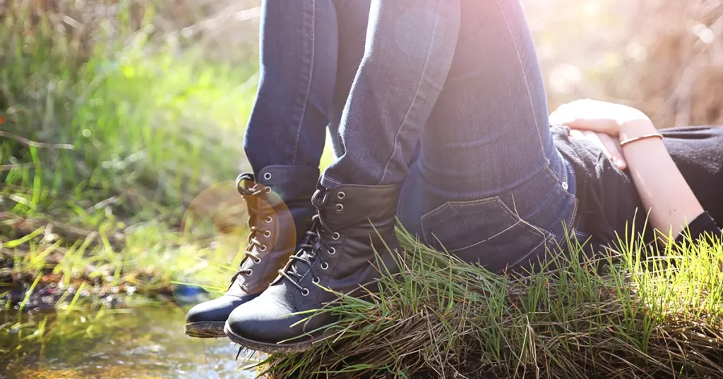girl lying on a small island in a stream with jeans and black combat boots on backlit