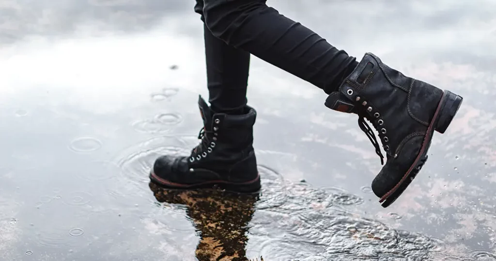 Girl wearing jeans and black combat boots splashing in a puddle after rain