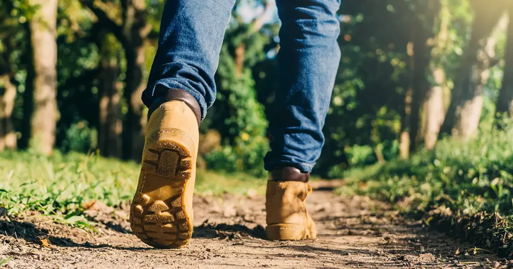 feet of an adult wearing boots to travel walking in a green forest. travel and hiking concept.