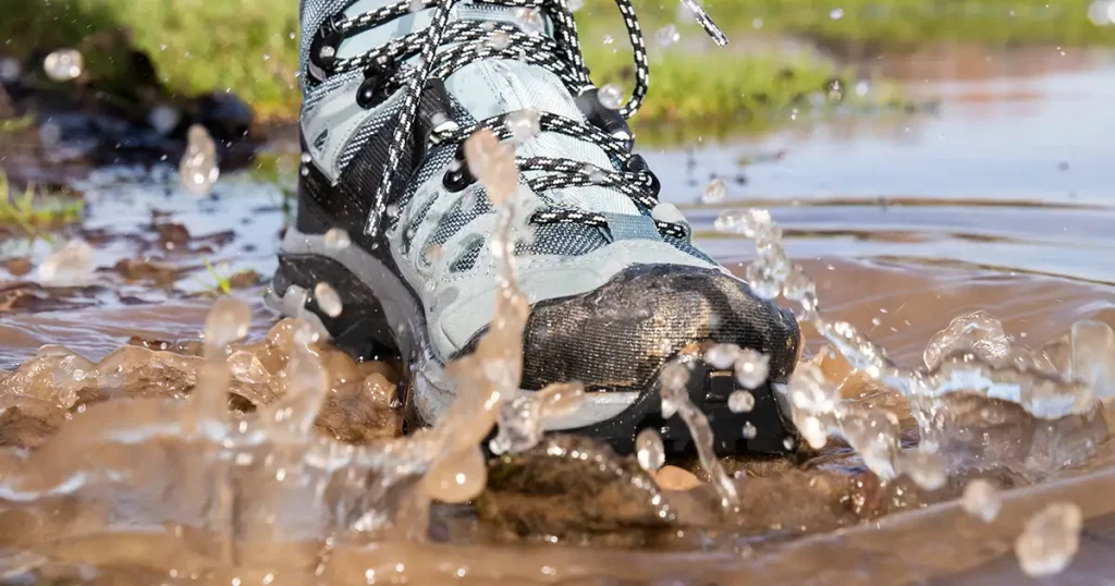 Hiking boot splashing in a puddle of muddy water