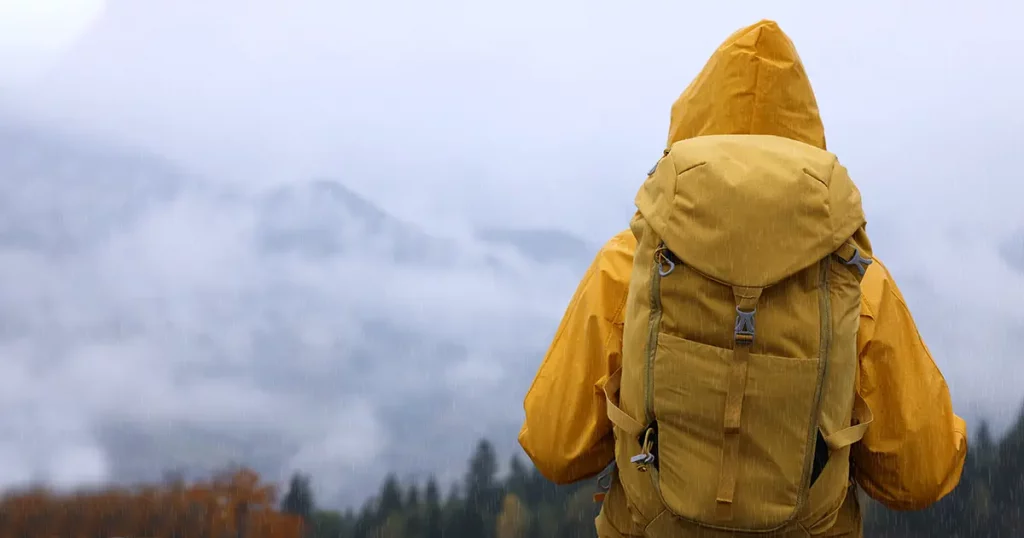 Woman in raincoat with backpack enjoying mountain landscape during rain, back view