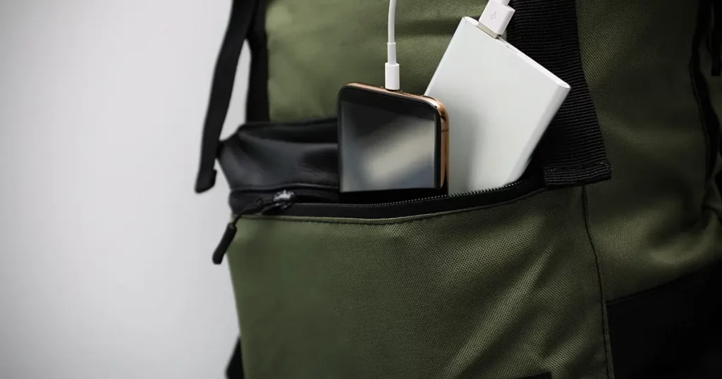 Smartphone charging with power bank in backpack on table, closeup