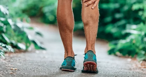 Man massaging sore calf muscles during running training outdoor from pain.