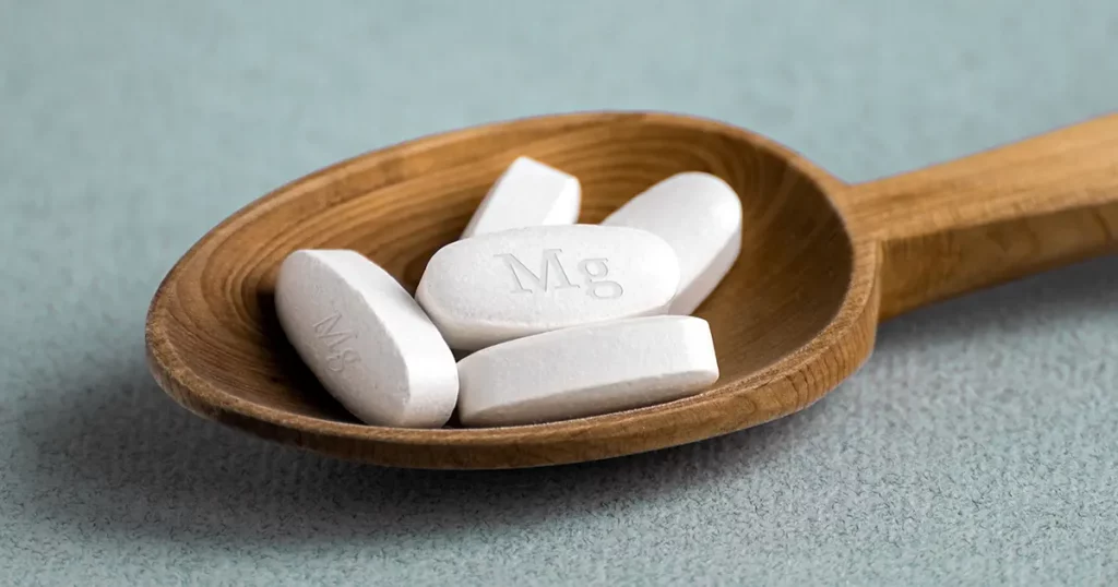Tablets , vitamins with the abbreviation Mg lying in a wooden spoon on a light background