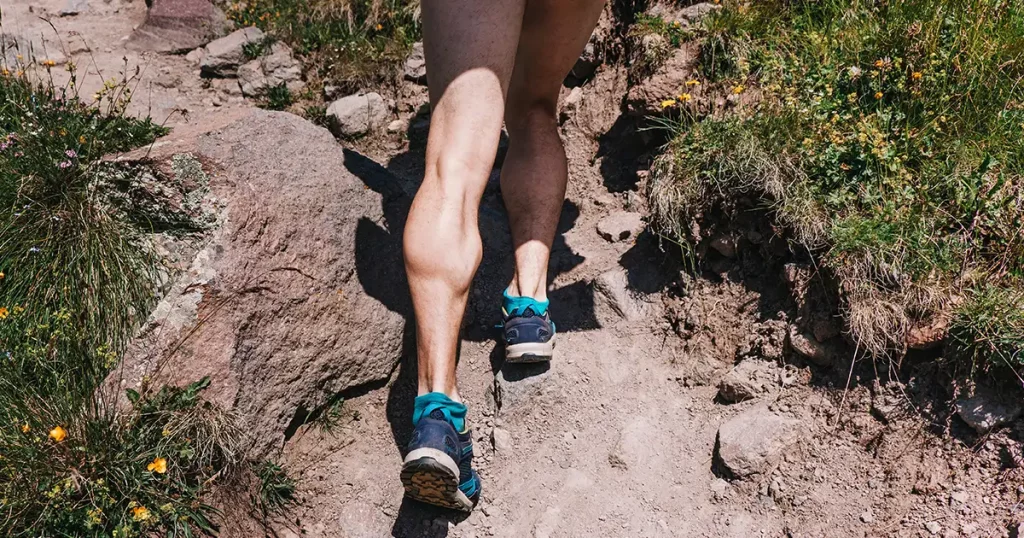 Muscular calves of a young athlete running up a mountain path, ultramarathon and skyranning