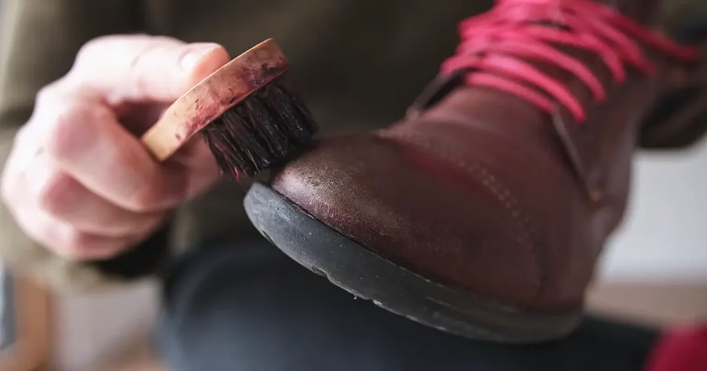Caucasian Male Using Soft Horsehair Brush to Apply Brown Shoe Shine Wax to Protect and Impregnate Leather Boots Shoes Wide