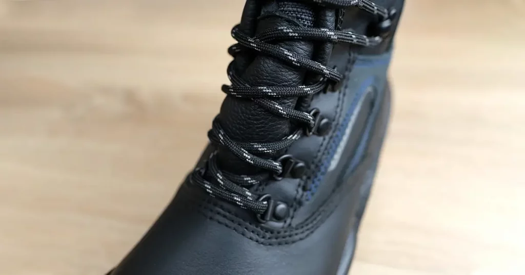 lose-up of one new black work boot with lacing made of leather with reinforced cape, high top on wooden floor