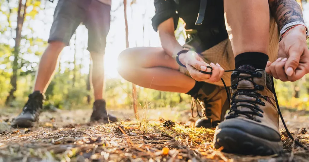 Close up of young female hiker tying shoelaces and getting ready for trekking in forest with man on background.