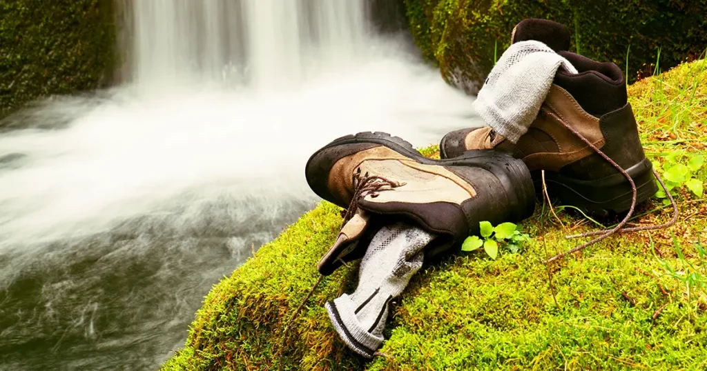 Hiker high boots and sweaty grey socks. Resting on the boulder at the nice mountain stream