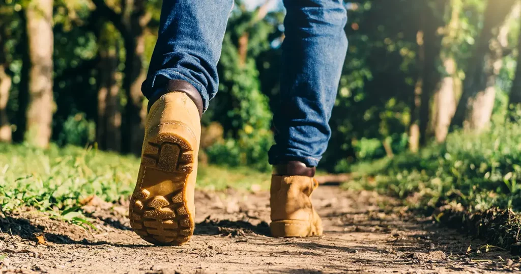 feet of an adult wearing boots to travel walking in a green forest. travel and hiking concept.