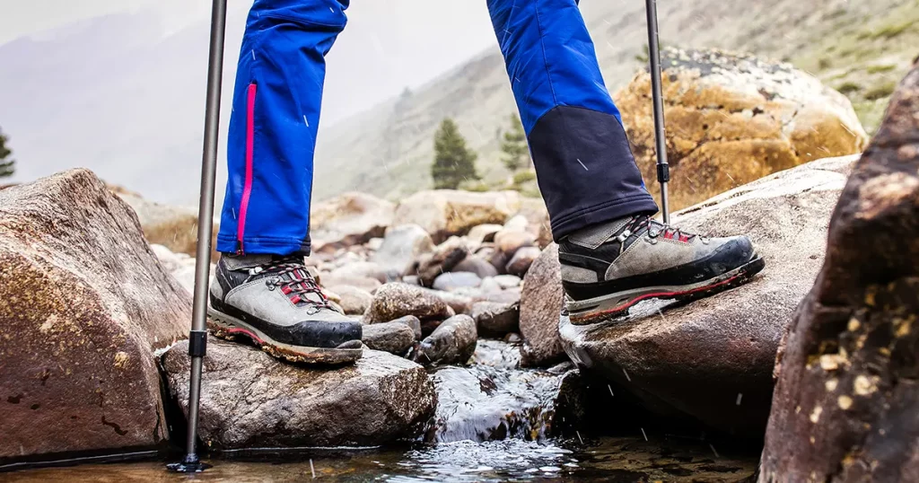 Waterproof trekking boots wade a rocky mountain stream
