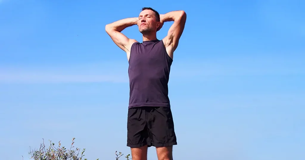 Runner athlete standing on summit of mountain, sunbathing and relaxing
