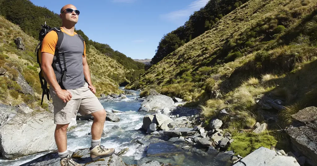 Full length of a male hiker standing by edge of a mountain river