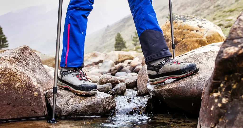 Waterproof trekking boots wade a rocky mountain stream.