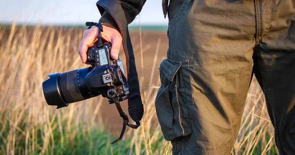 Photographer holding digital camera outdoors. Hiking man photographing landscape.