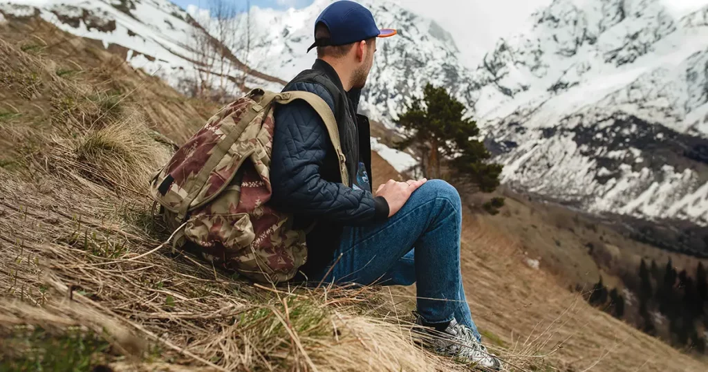 young hipster man sitting in mountains, swag outfit, winter vacation