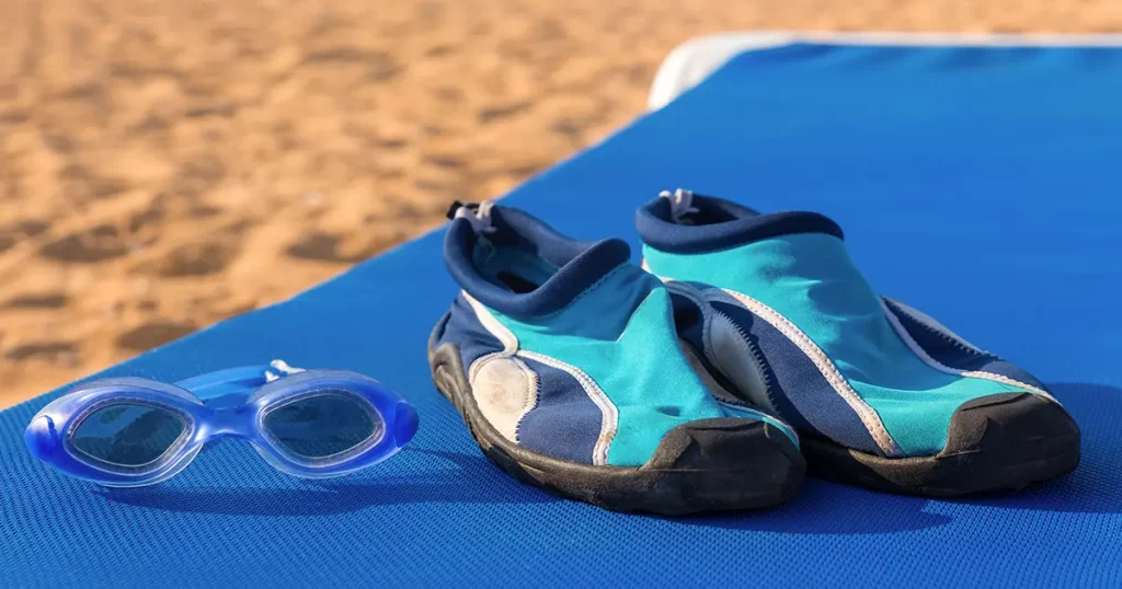 Swimming goggles with water shoes on a beach bed by the sea
