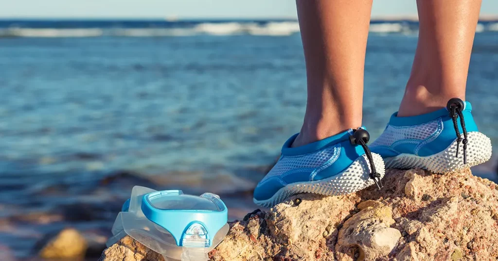 Female feet in aqua shoes near reefs and corals . Water sports equipment.