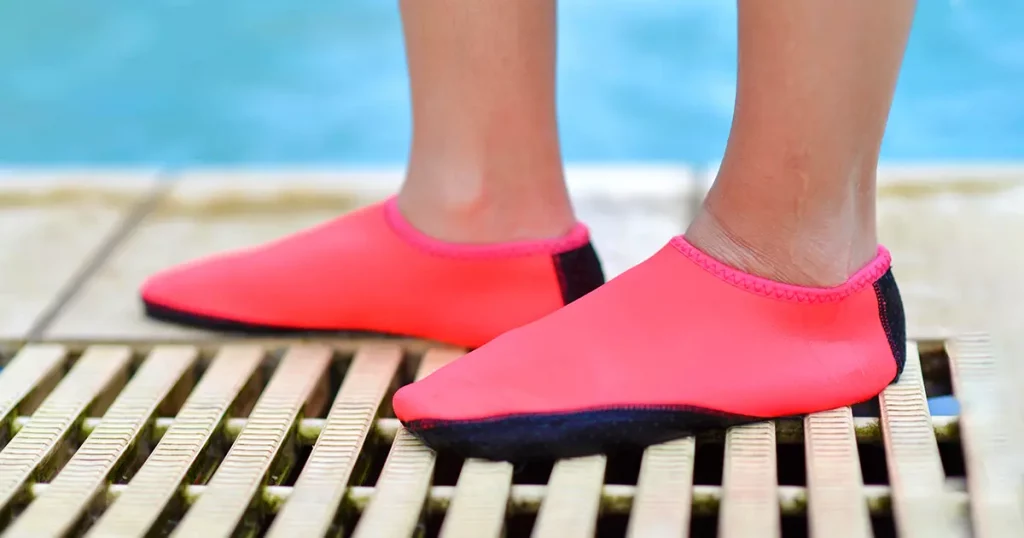 Legs with pink swimming footwear.Young girl's feet wearing swim shoes by the pool.